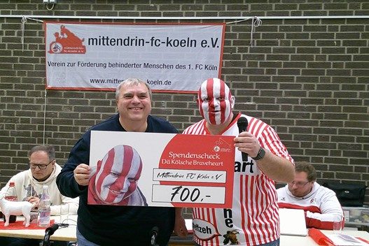Zwei Männer halten einen großen Scheck in einem festlichen Umfeld.
