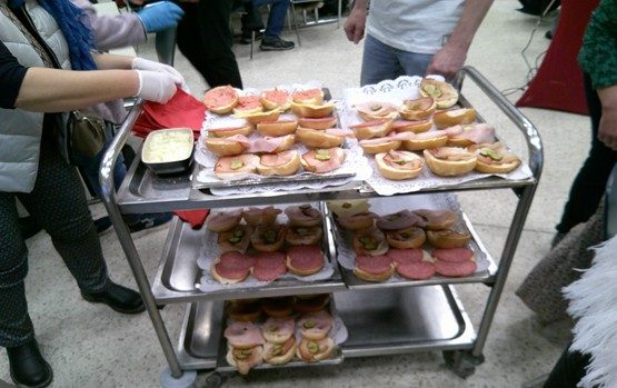 Ein Rollwagen mit belegten Brötchen und Aufschnitt, umgeben von Menschen.