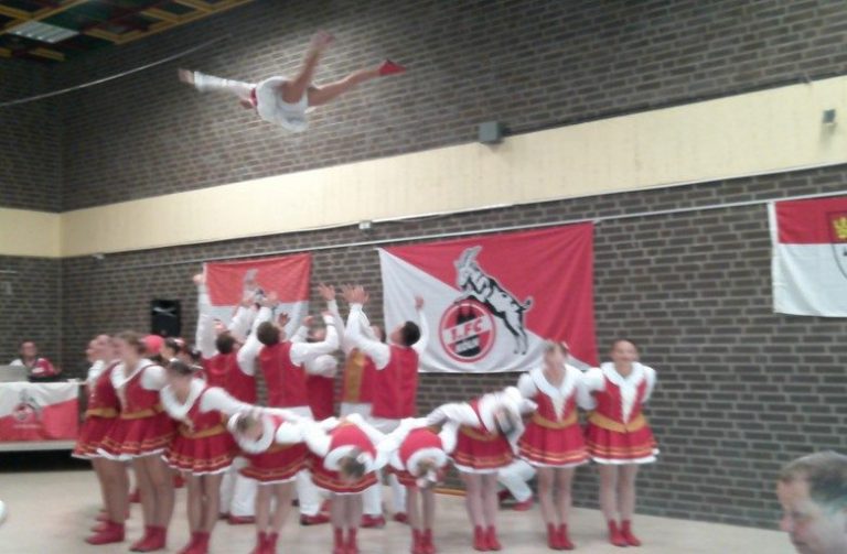 Tanzgruppe in roten Uniformen, während ein Mitglied in die Luft springt.