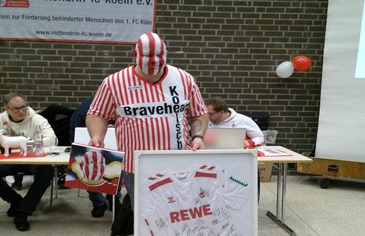 Ein Fußballfan mit gestrichener Gesichtsfarbe trägt ein rotes und weißes Trikot und präsentiert sein Geschenk